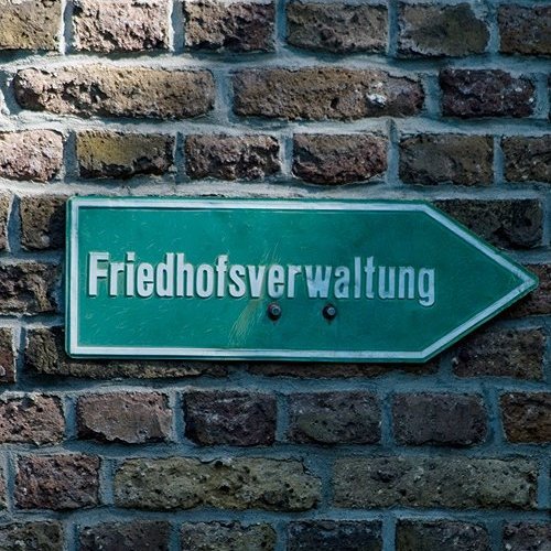 Schild mit der Aufschrift Friedhofsverwaltung an einer Ziegelmauer