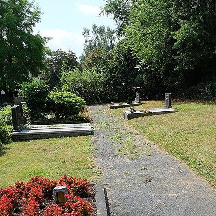 Einzelne Gräber auf fast leerer Fläche an einem Weg auf einem Friedhof