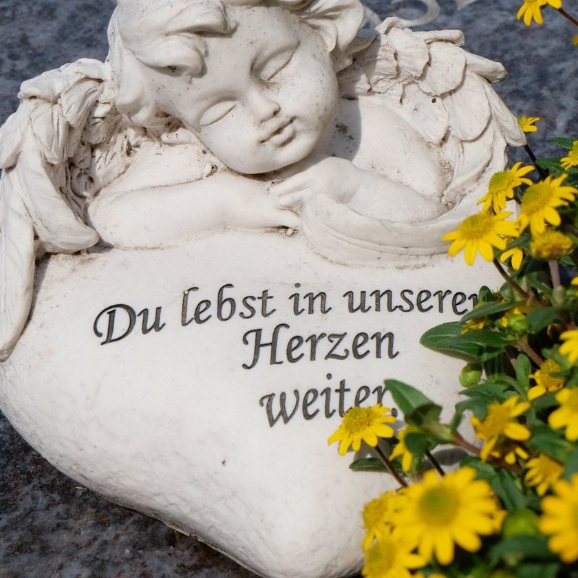 Weiße Engelfigur und gelbe Blumen auf einer steineren Grabplatte
