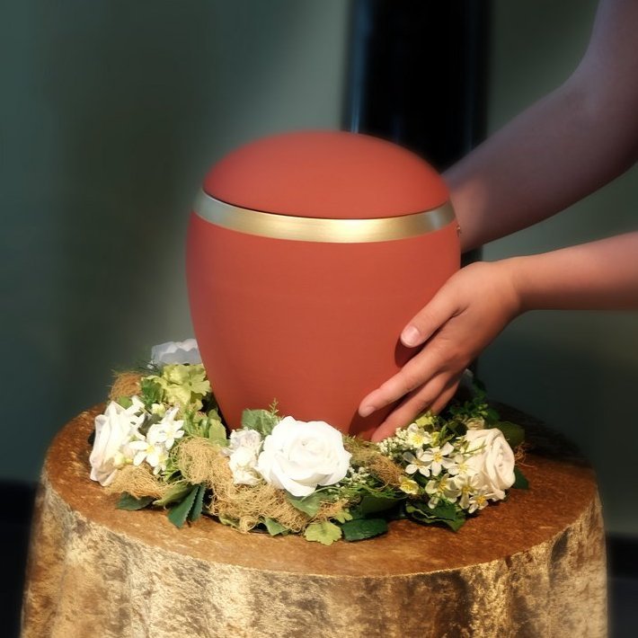 Frau stellt eine rote Urne auf einen mit Tuch und Blumen geschmückten Ständer